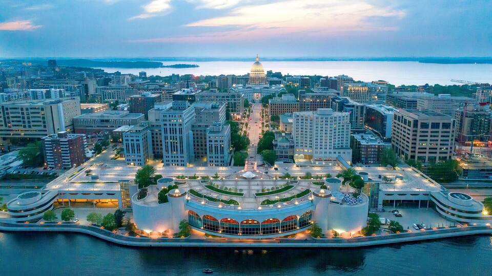 A cityscape with a prominent circular building with a dome, surrounded by modern architecture and a waterfront.