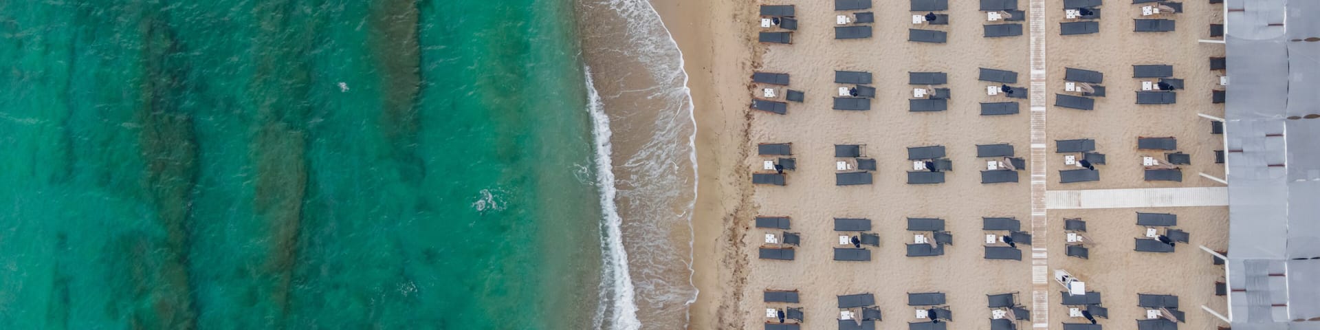 An aerial view of a beach with rows of beach huts and a clear turquoise sea.