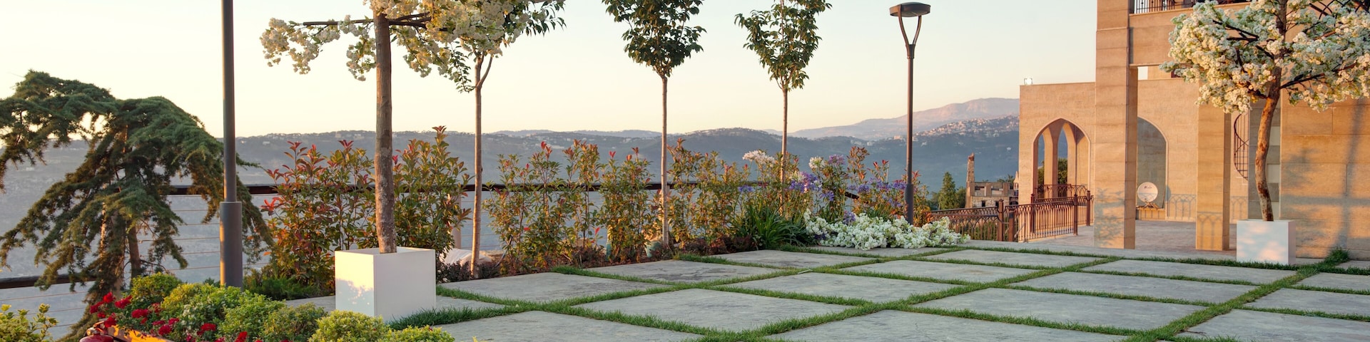 A landscaped garden with a wooden bench, flowering plants, and a building with arched windows.