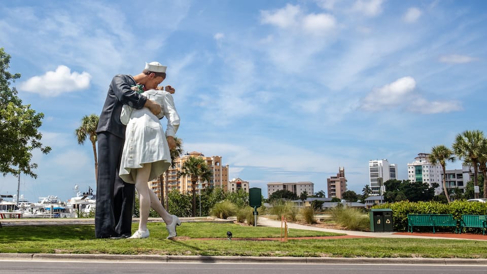 A statue of a man and woman embracing on a grassy area with a cityscape in the background.