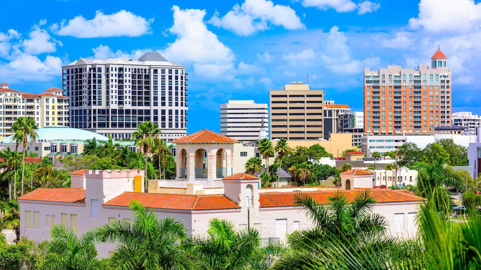A cityscape with a mix of modern and historic buildings, palm trees, and a clear blue sky.