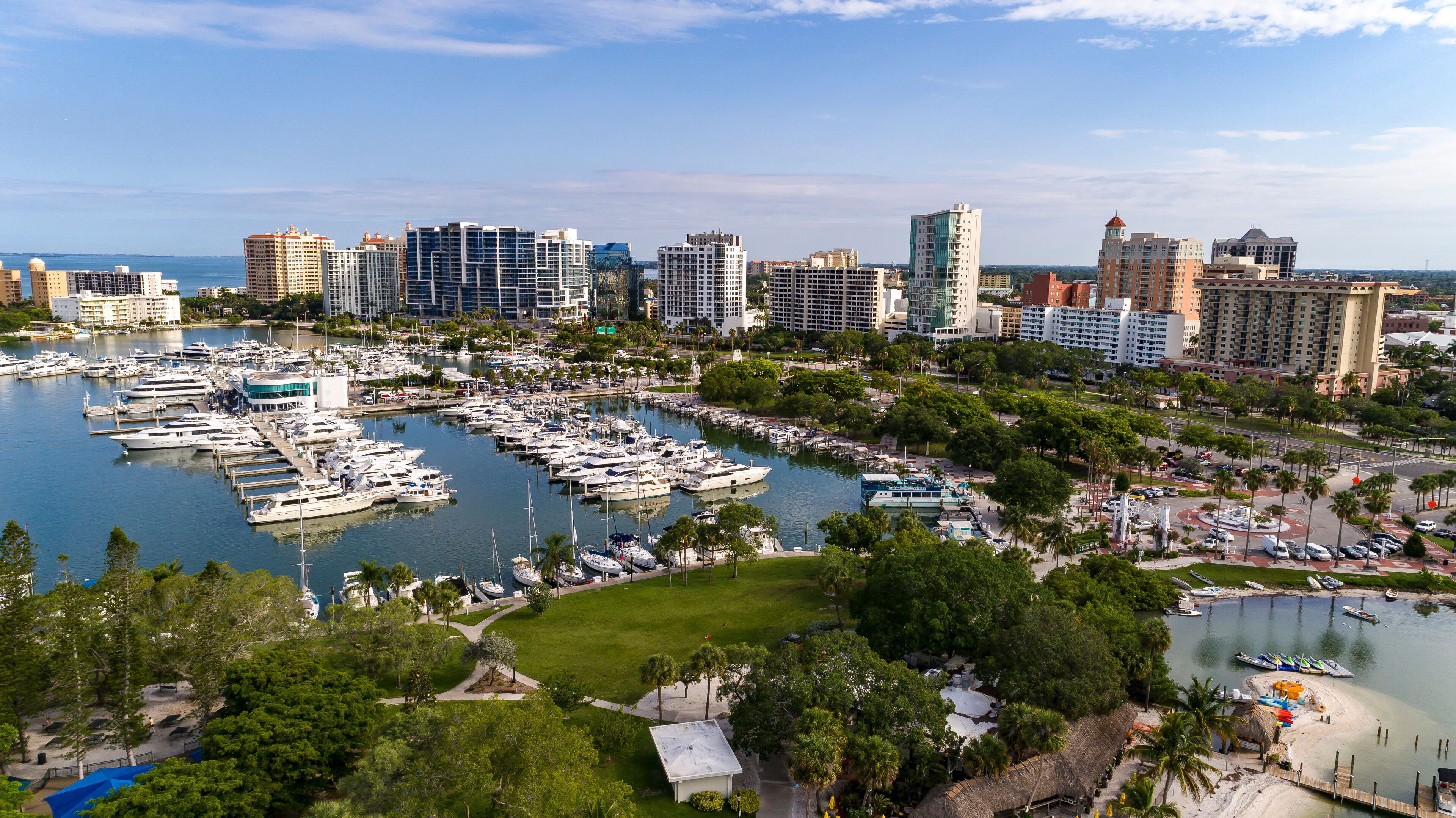 A marina with yachts, a marina with boats, and a city skyline with tall buildings.