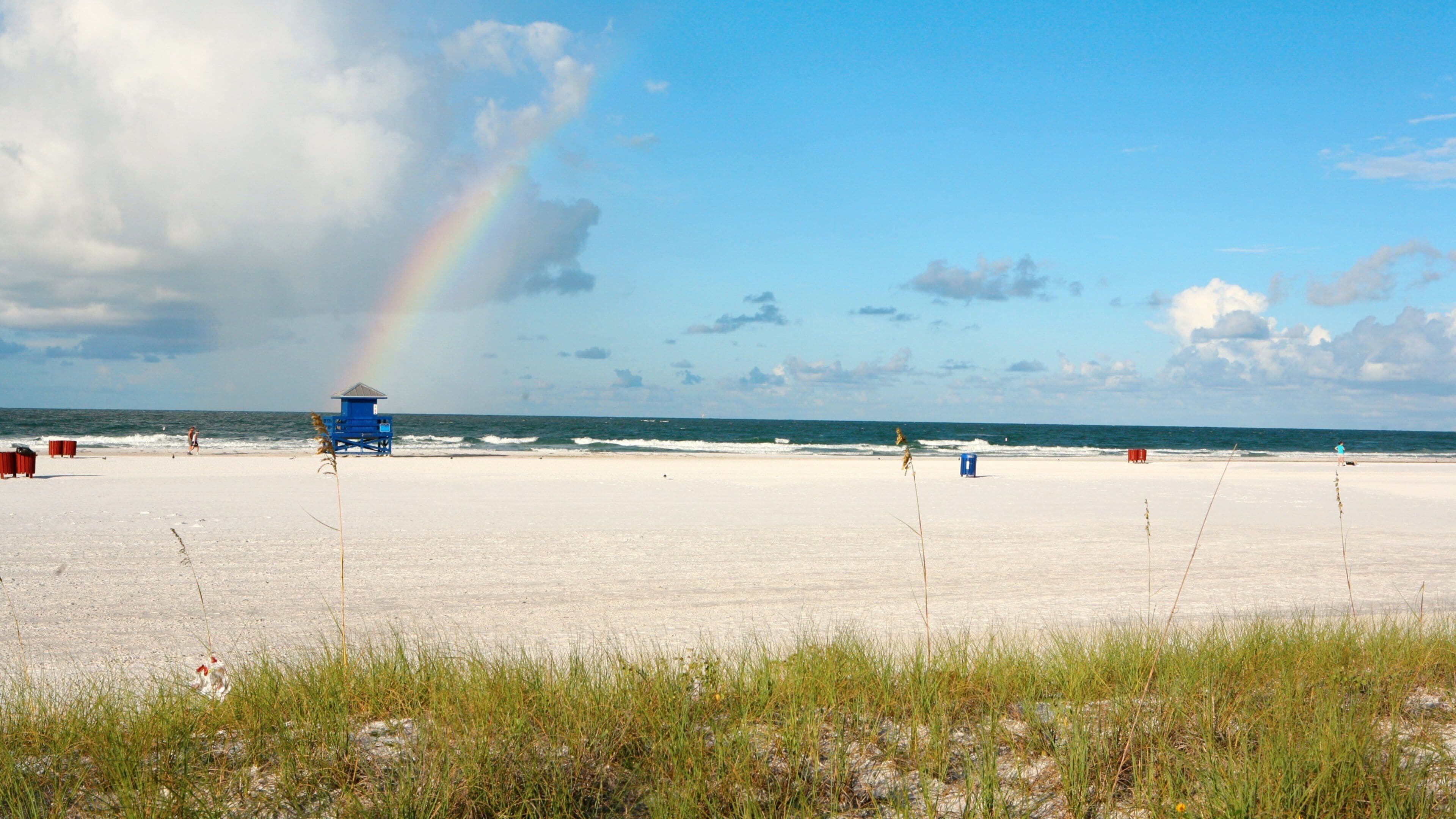 A beach with a lifeguard tower, ocean waves, and a rainbow.
