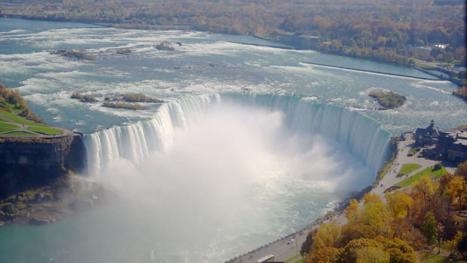 A large waterfall with a river flowing around it, surrounded by trees and a small town.