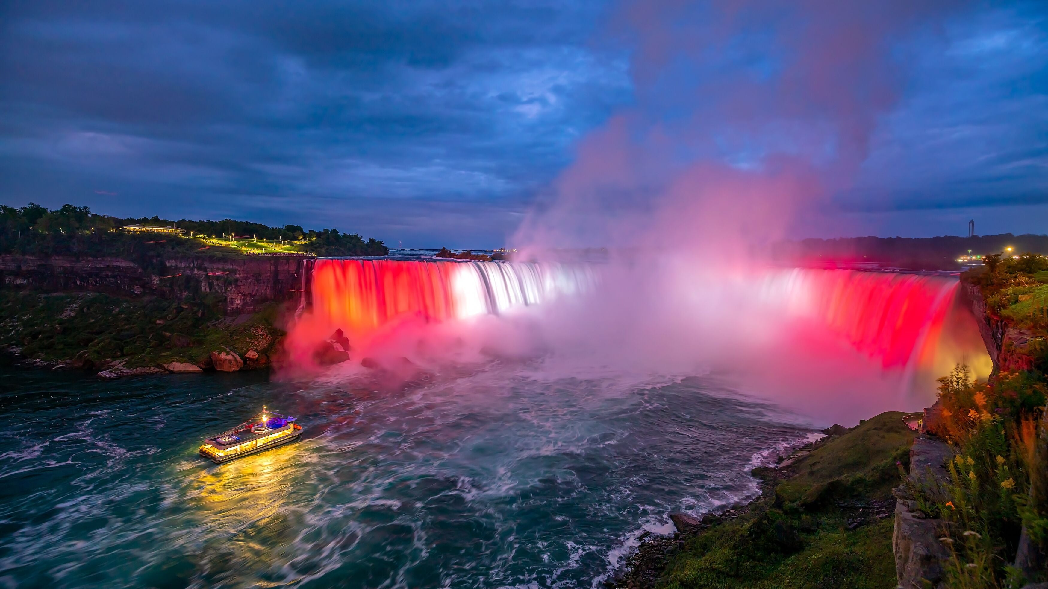 Una cascada con una barca en primer plano y un edificio iluminado al fondo.