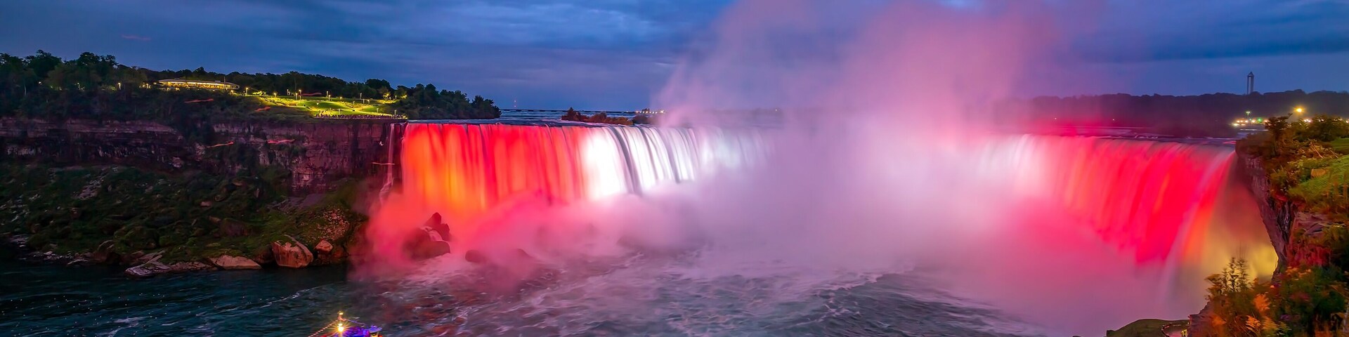 Una cascada con una barca en primer plano y un edificio iluminado al fondo.