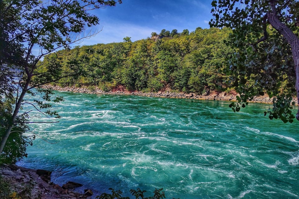 Un riu d'aigua turquesa envoltat de bosc verd i dens, i terreny rocos.