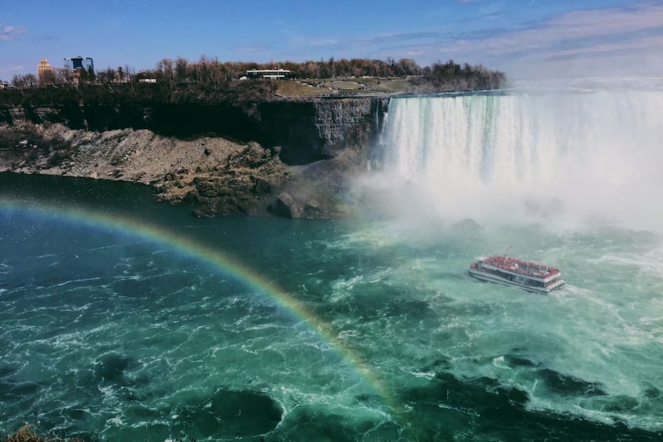Une grande cascade avec un arc-en-ciel, un bateau et une rive rocheuse.