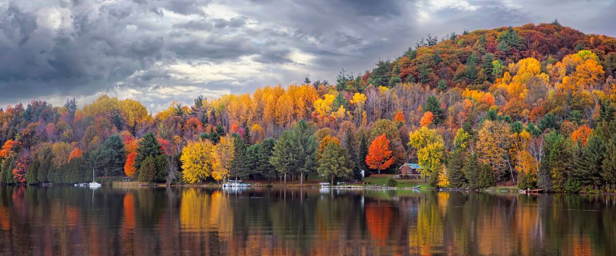 A lake surrounded by autumn-colored trees and a cloudy sky.