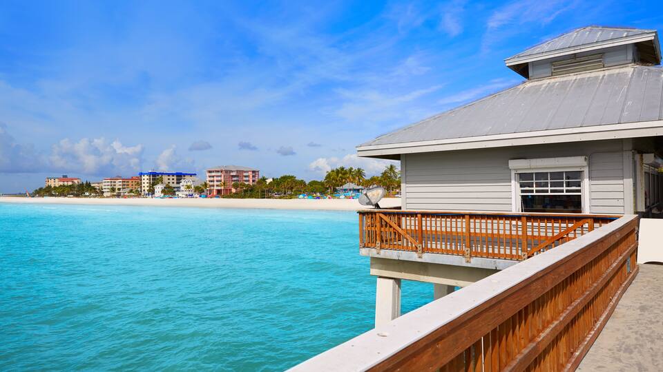 A wooden deck overlooking turquoise ocean waters with a beach and buildings in the background.