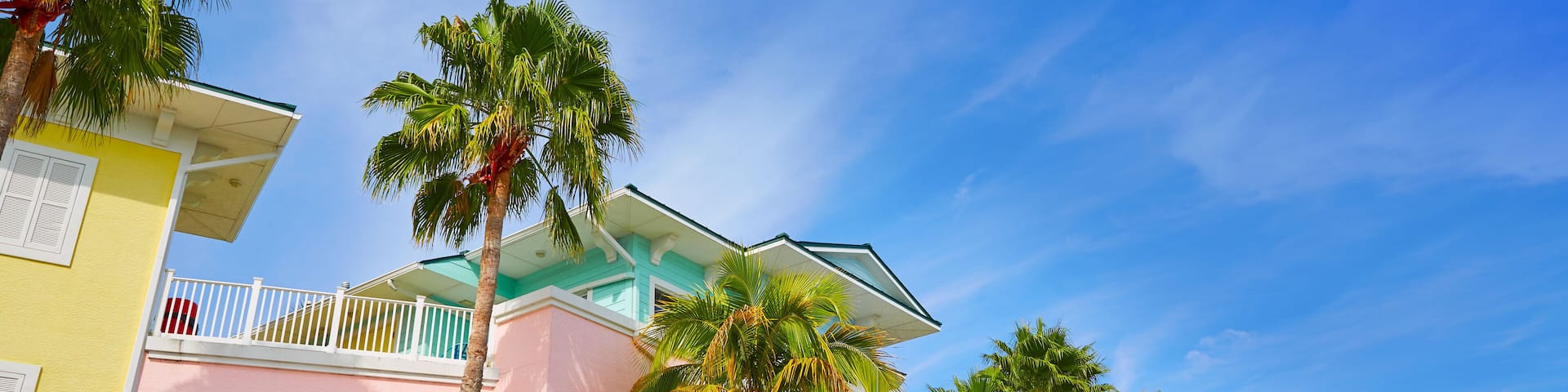 A colorful row of pastel-colored buildings with balconies and palm trees.