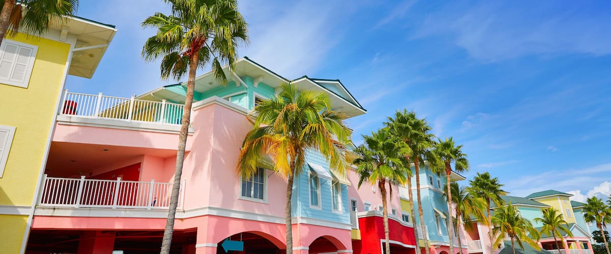 A colorful row of pastel-colored buildings with balconies and palm trees.