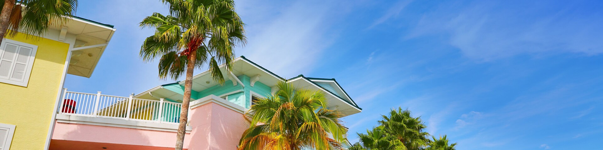 A colorful row of pastel-colored buildings with balconies and palm trees.