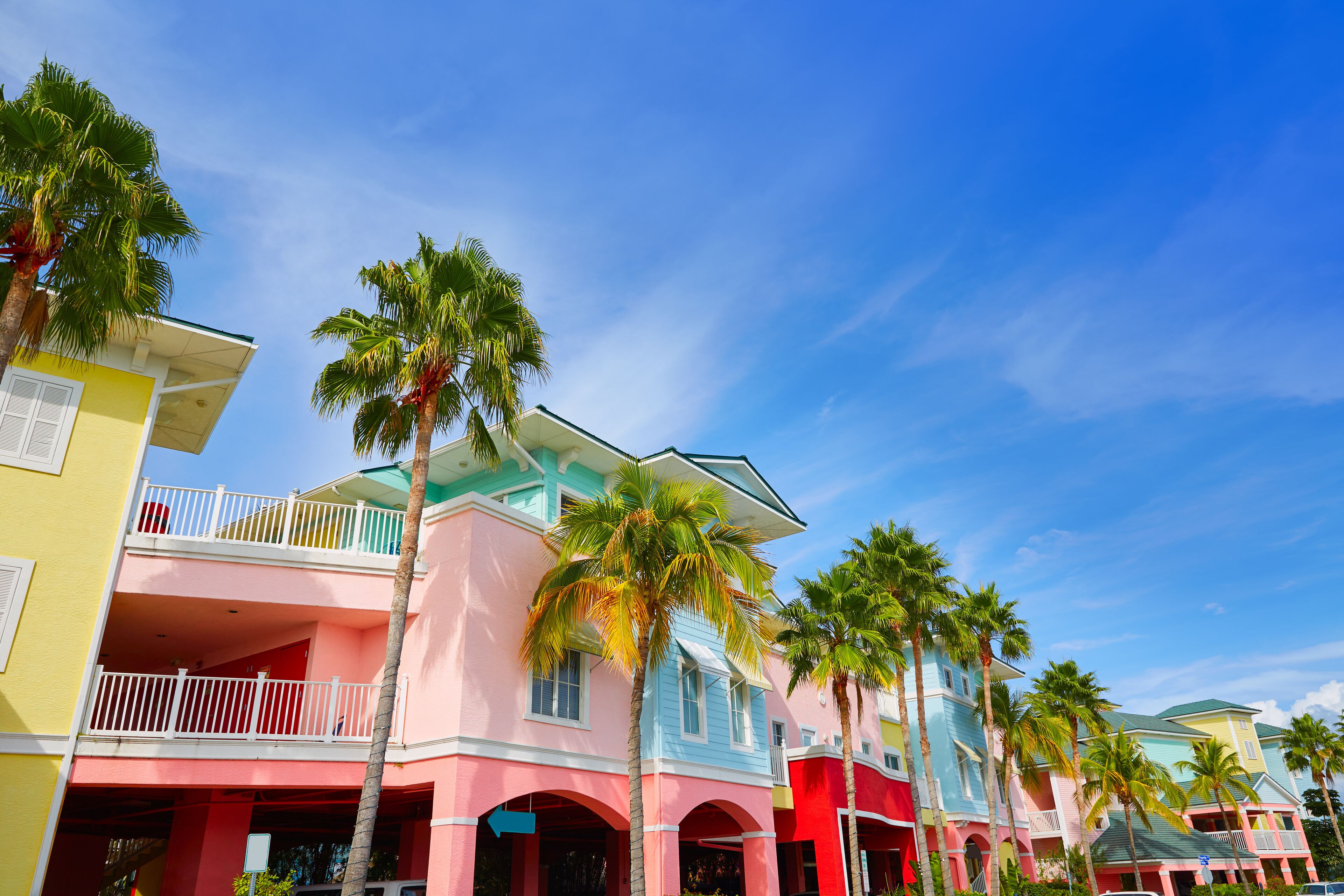 A colorful row of pastel-colored buildings with balconies and palm trees.