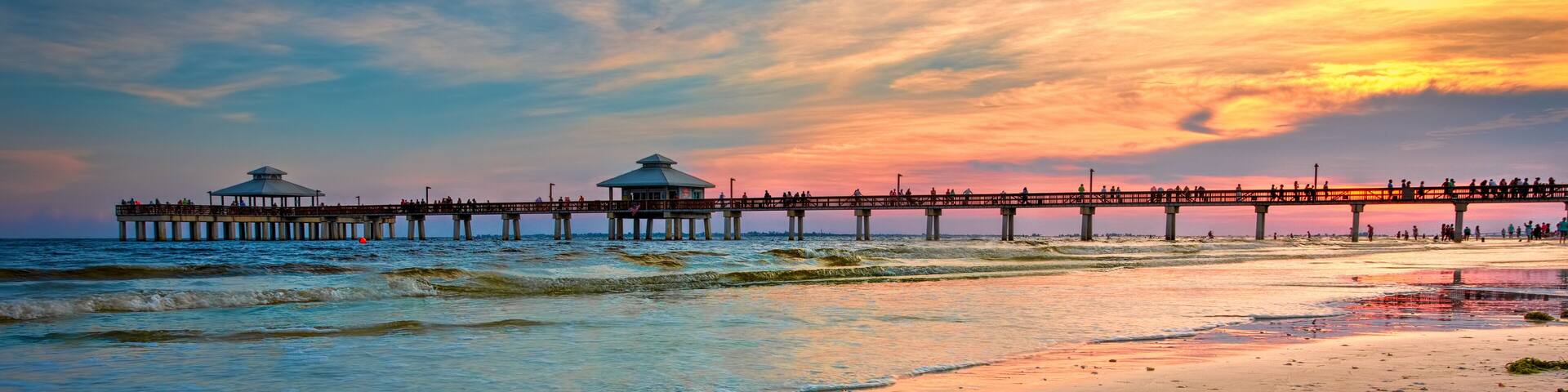 A beach with a pier extending into the ocean, featuring a gazebo and people walking.