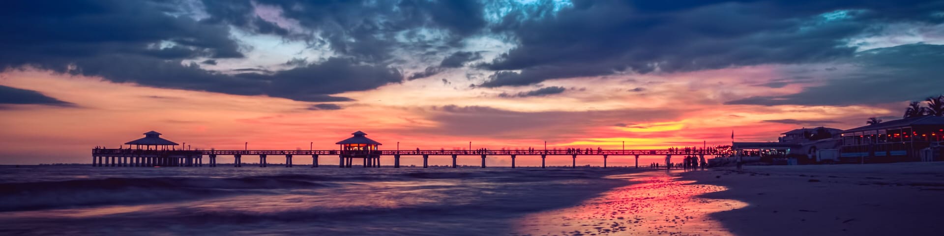 Un atardecer sobre una playa con un muelle que se adentra en el agua.