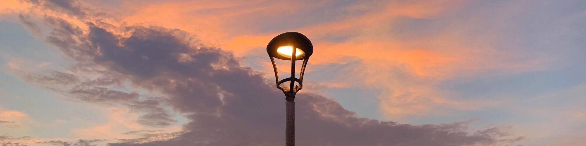 Un coucher de soleil sur l’océan, avec un lampadaire et des bancs le long de la plage.