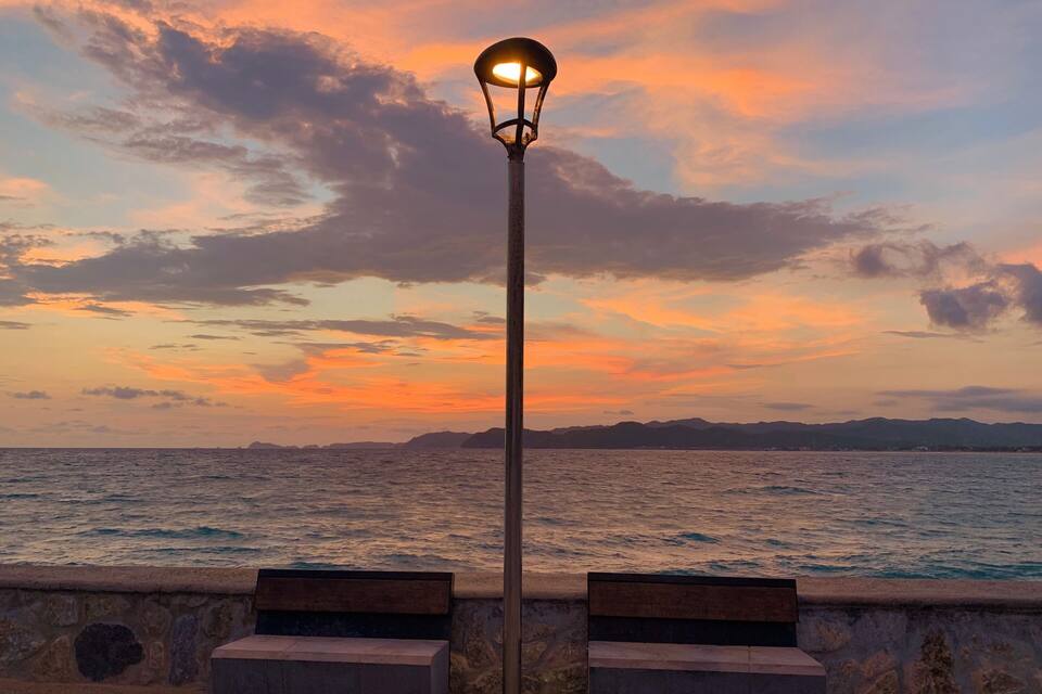 Una puesta de sol sobre el océano, con una farola y bancos a lo largo de la orilla.