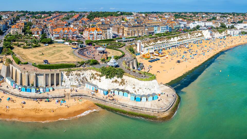 An aerial view of a coastal town with a sandy beach, a promenade, and a variety of buildings along the shore.