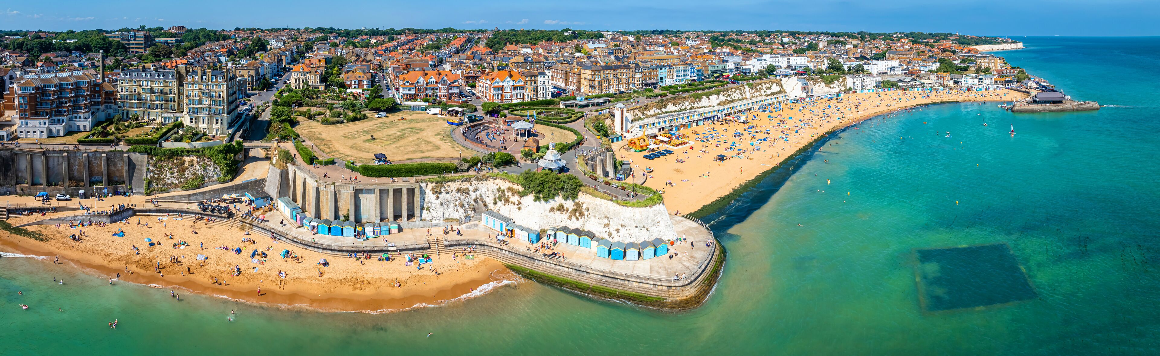 An aerial view of a coastal town with a sandy beach, a promenade, and a variety of buildings along the shore.