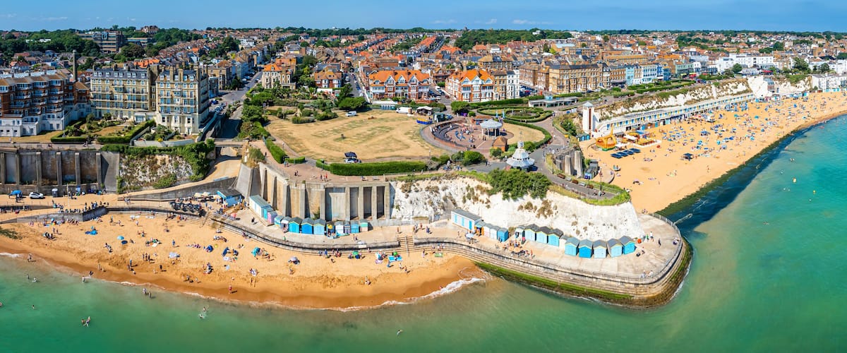 An aerial view of a coastal town with a sandy beach, a promenade, and a variety of buildings along the shore.