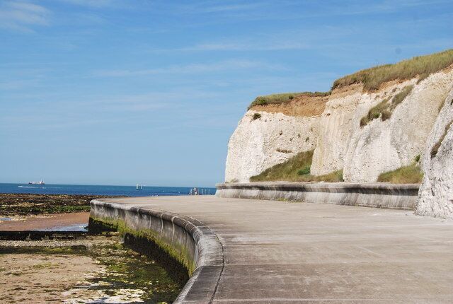 A coastal walkway with white cliffs and a sandy beach.
