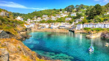 A coastal town with houses on a hillside, a clear blue harbor, and a sailboat.