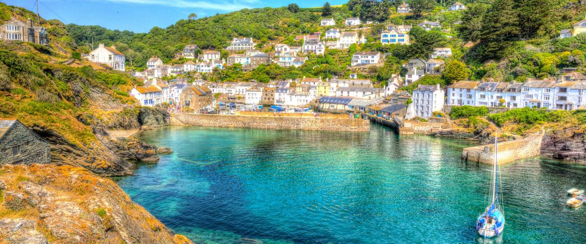 A coastal town with houses on a hillside, a clear blue harbor, and a sailboat.