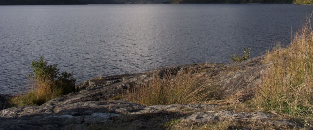 A calm lake surrounded by mountains and grassy hills.