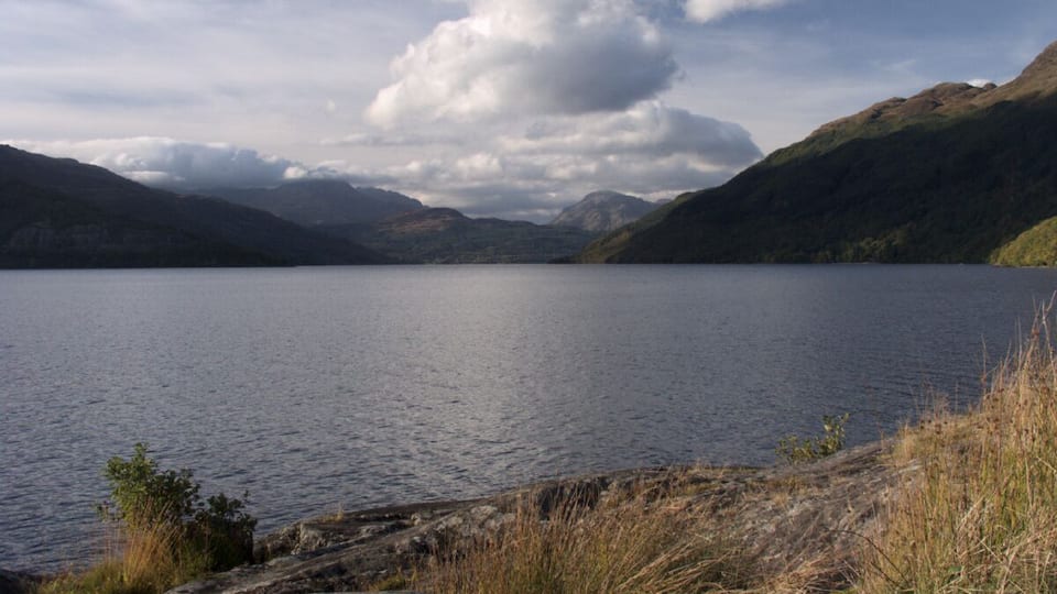A calm lake surrounded by mountains and grassy hills.