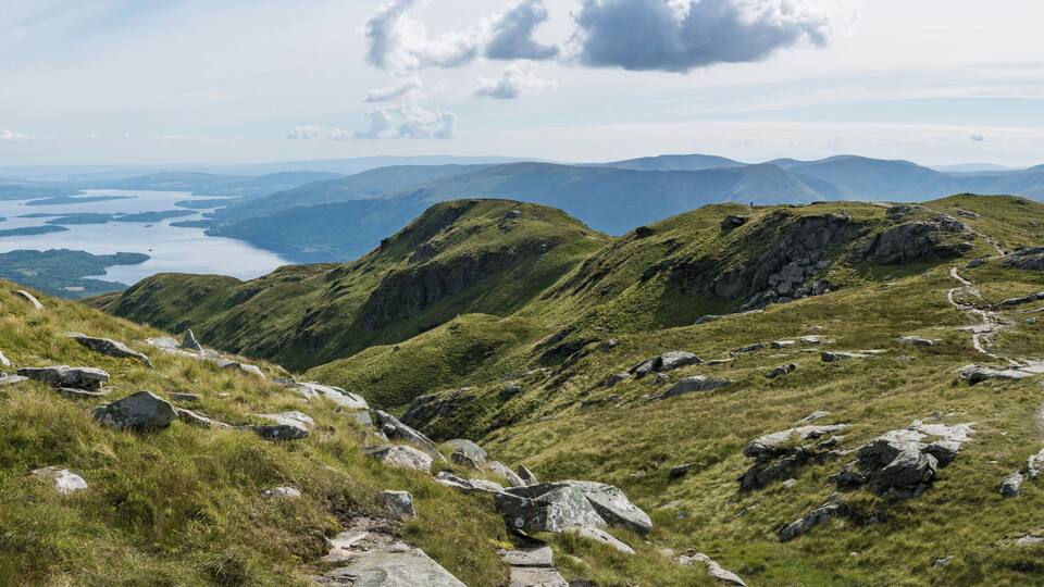 A mountainous landscape with a winding path, rocky outcrops, and a distant lake.