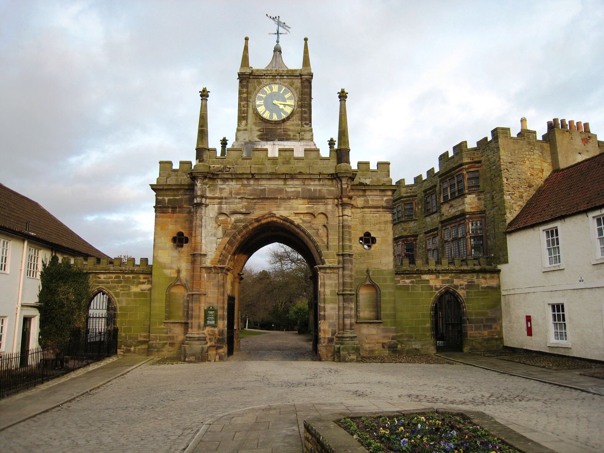 A historic stone archway with a clock tower, surrounded by traditional buildings.