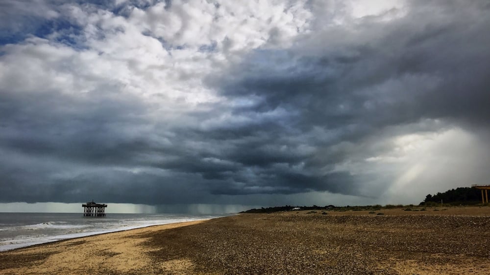 A beach with a pier extending into the ocean under a stormy sky.