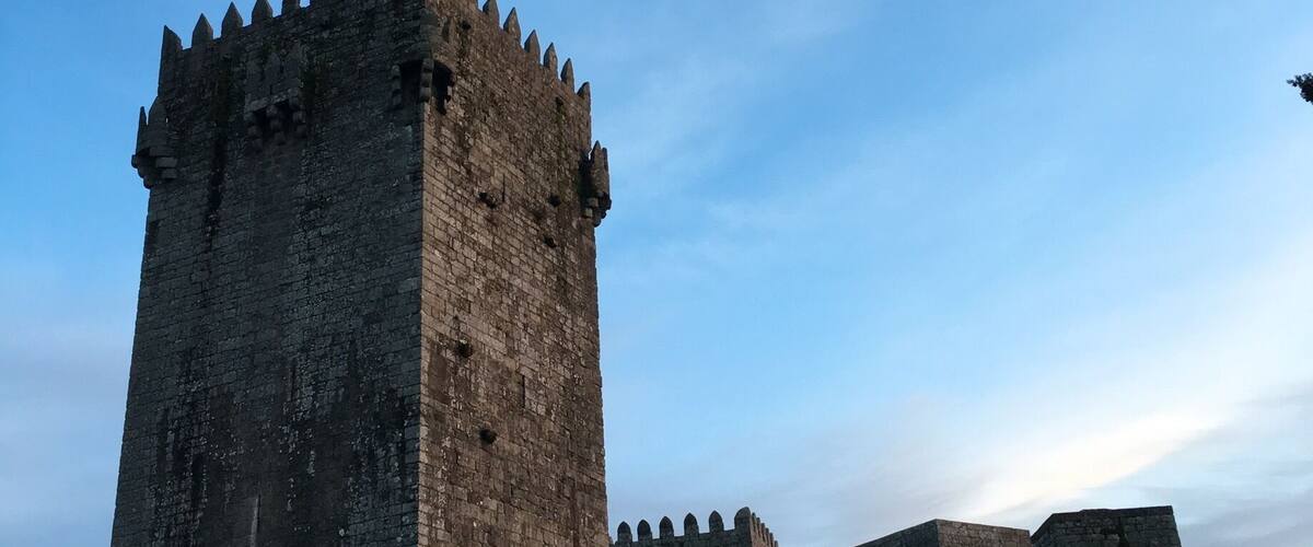 A medieval castle with a tall central tower and smaller towers, surrounded by a grassy area.