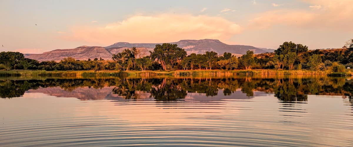 A calm lake with reflections of trees and mountains in the background.
