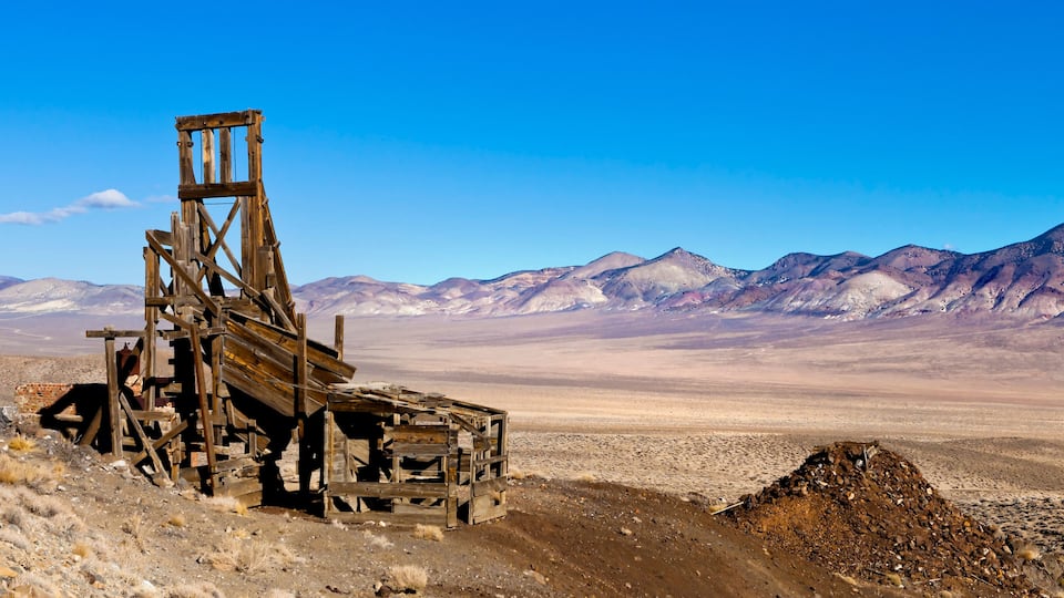 A dilapidated wooden structure in a barren landscape with mountains in the background.