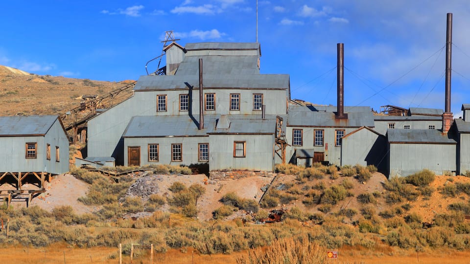 A dilapidated industrial complex with rusted metal buildings and chimneys, set against a desert landscape.