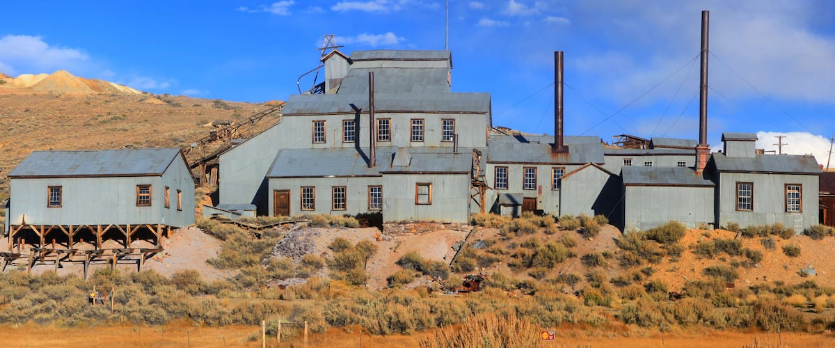 A dilapidated industrial complex with rusted metal buildings and chimneys, set against a desert landscape.