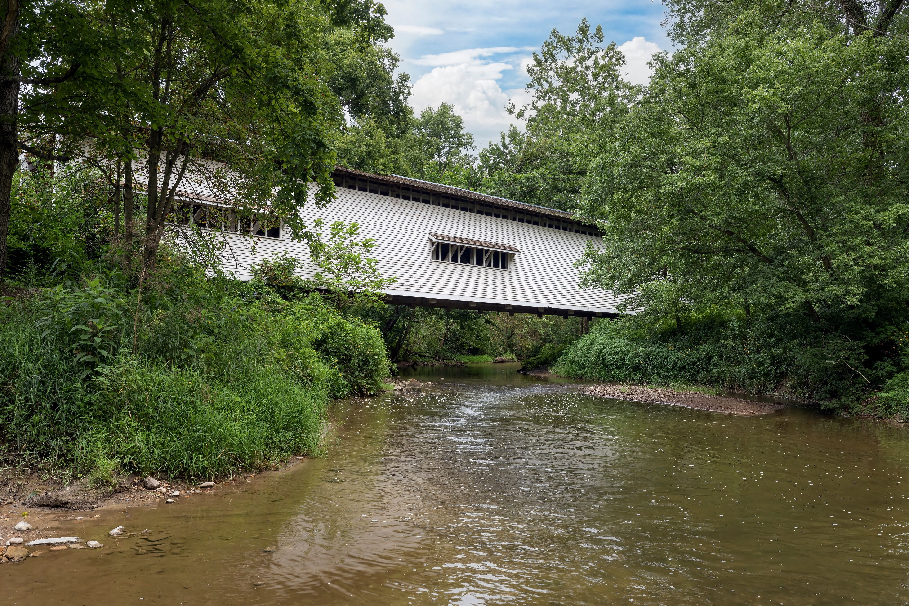Built in 1856, the historic white Portland Mills Covered Bridge now crosses Little Raccoon Creek in Parke County, Indiana.