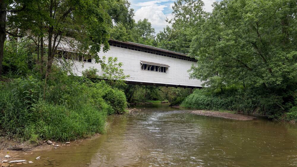 Built in 1856, the historic white Portland Mills Covered Bridge now crosses Little Raccoon Creek in Parke County, Indiana.