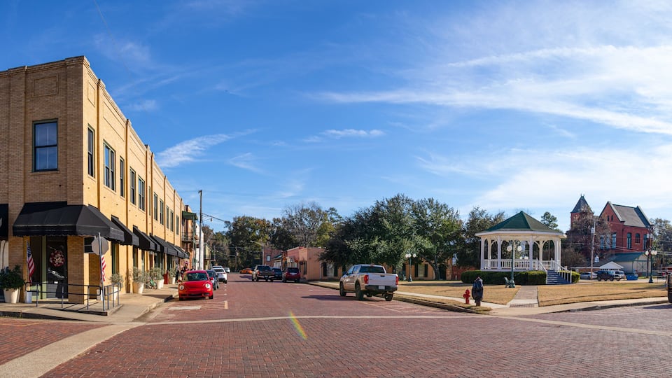 A brick-paved street with a gazebo, a red car, and a white pickup truck.