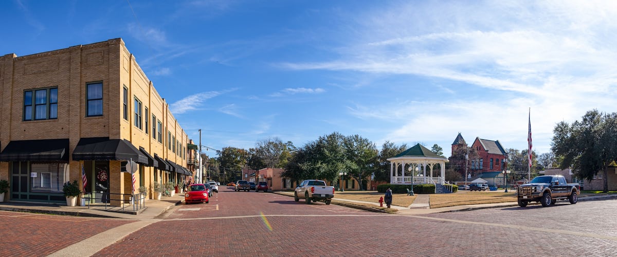 A brick-paved street with a gazebo, a red car, and a white pickup truck.