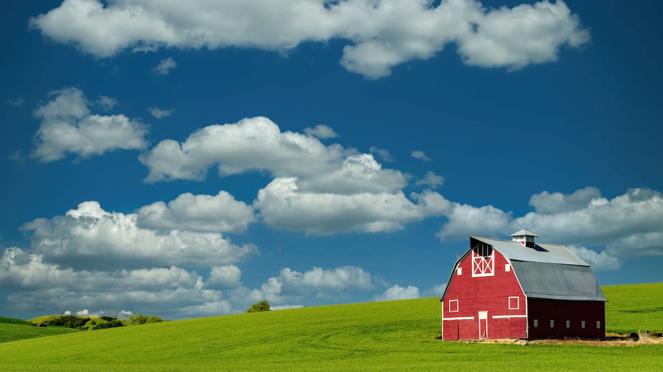 A red barn on a green hill under a blue sky with clouds.