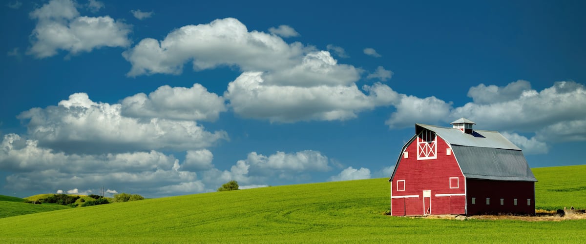 A red barn on a green hill under a blue sky with clouds.