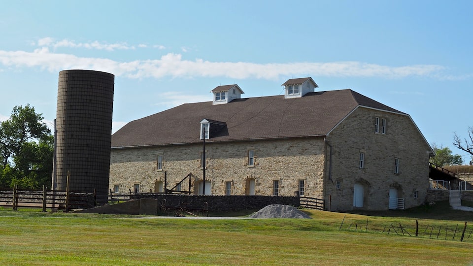 A large stone barn with a silo, surrounded by a grassy field and a wooden fence.