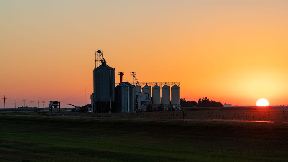 A grain silo complex silhouetted against a sunset.