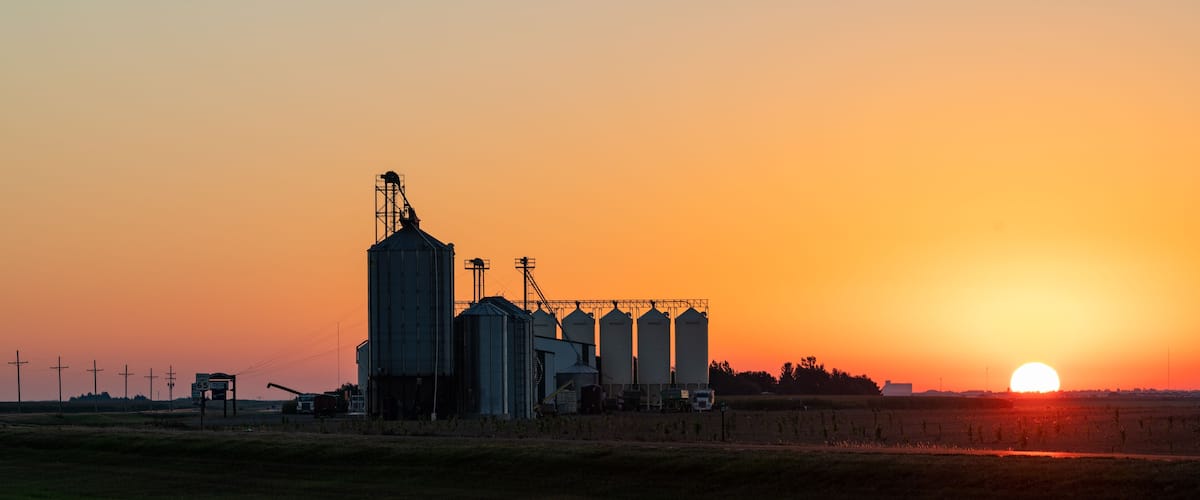 A grain silo complex silhouetted against a sunset.