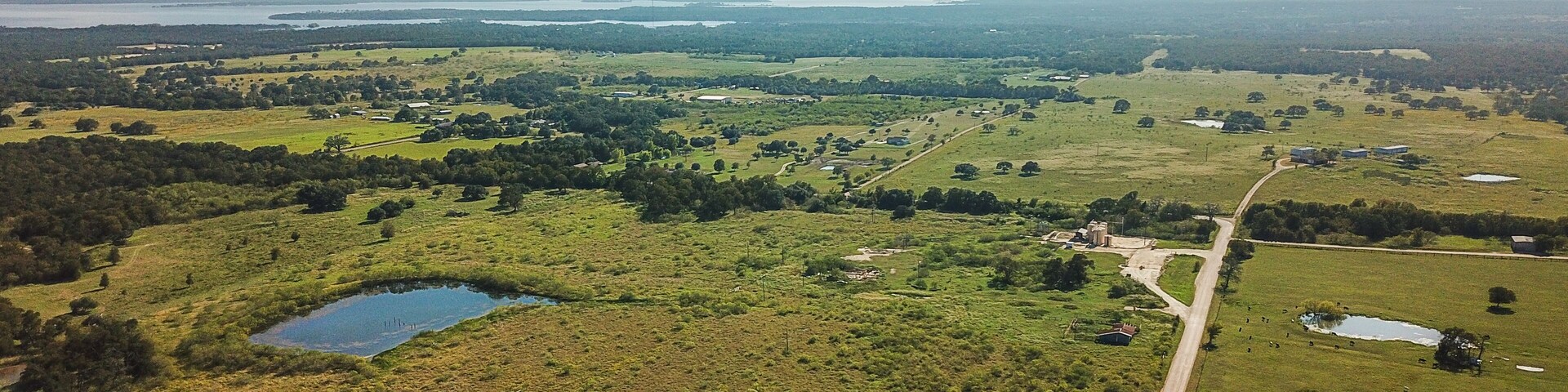 Vista aérea de un paisaje rural con campos, un lago pequeño y edificios dispersos.