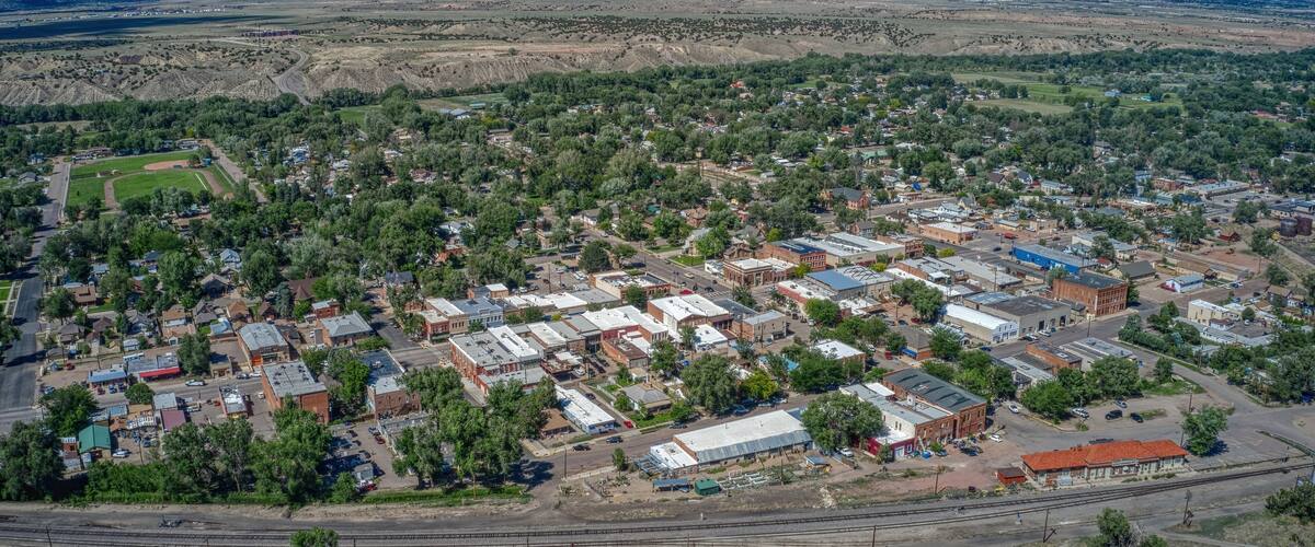 An aerial view of a town with a mix of residential and commercial buildings, surrounded by green areas and a railway line.