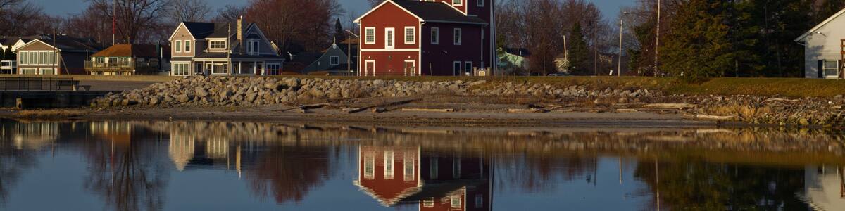 A calm lake reflecting a red building with a tower, surrounded by trees and other houses.